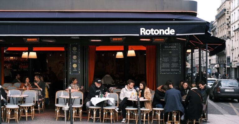Bustling Paris café with outdoor seating and people enjoying meals on a city street.