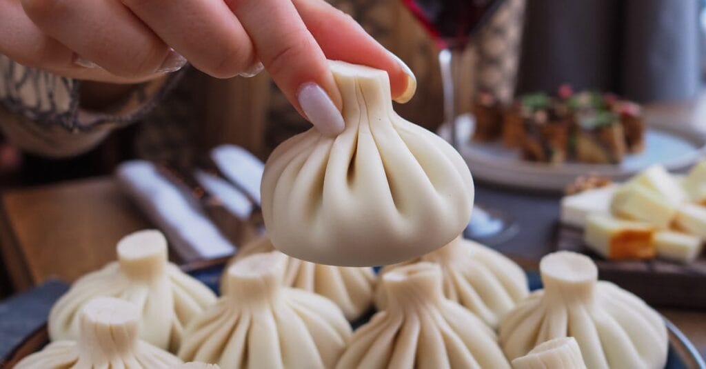 Close-up of a woman picking khinkali dumplings with a glass of red wine on the table.
