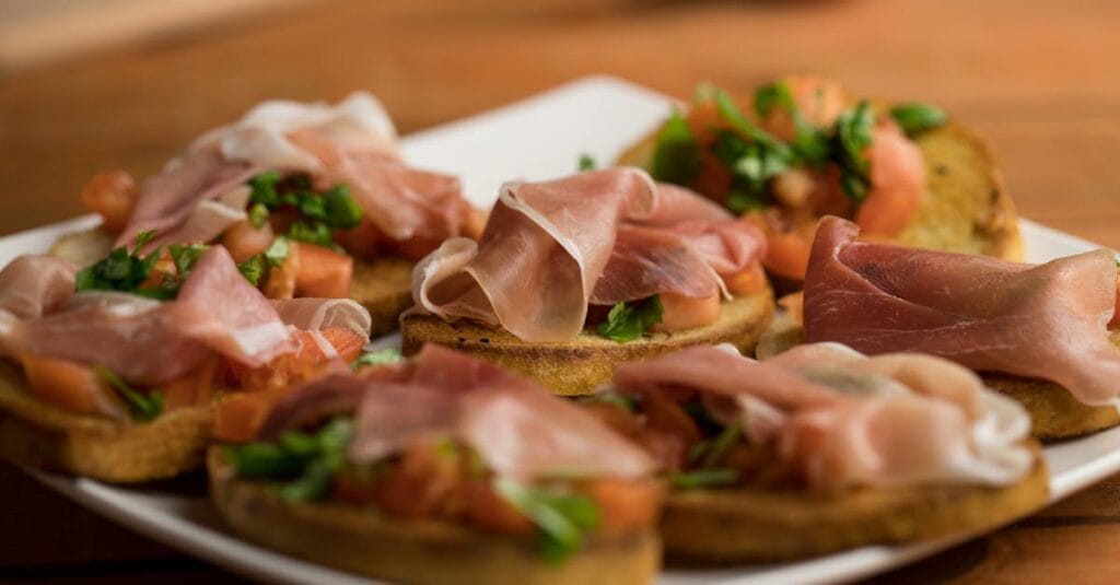 Delicious Italian bruschetta topped with prosciutto and fresh herbs on a wooden table.