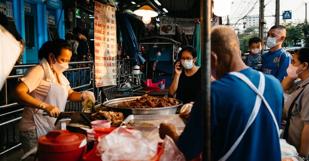 Market vendor selling food at a street market in Bangkok, with people wearing face masks.