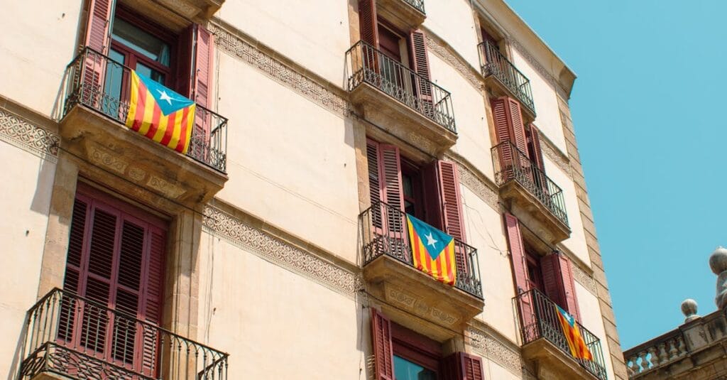 A low-angle view of a historic building facade in Barcelona displaying Catalan flags.