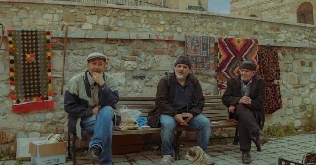 Three men on a bench showcasing traditional carpets in Kütahya, Turkey.