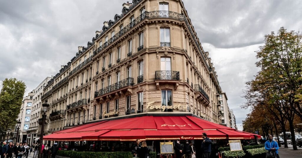Charming Parisian restaurant with red awnings and classic architecture under a cloudy sky.