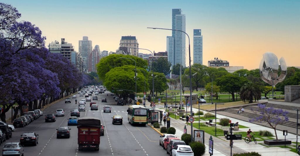 View of a bustling Buenos Aires avenue lined with trees under a clear sky, showcasing city life and iconic landmarks.