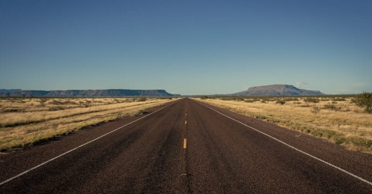A tranquil desert highway stretching through Terlingua, Texas under a clear blue sky.