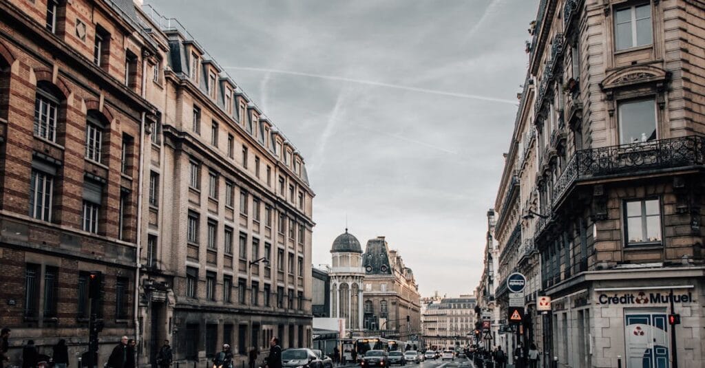 Urban street scene in Paris with classic architecture, cars, and pedestrians on an overcast day.