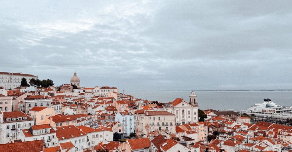 Discover Lisbon's charm with this elevated view of historic rooftops and the sea, capturing Portugal's essence.