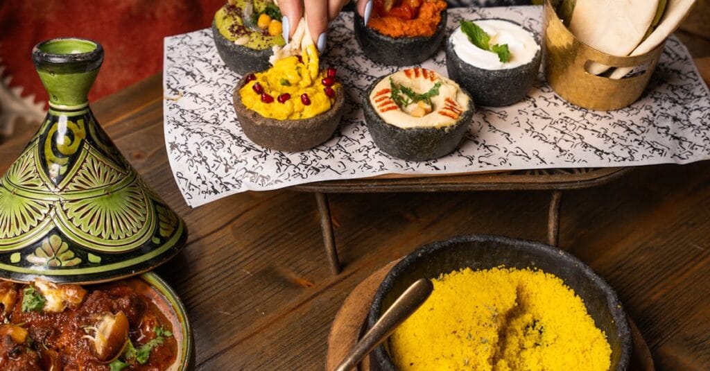 A vibrant Moroccan meal featuring beef tagine, various dips, bread, and yellow couscous, perfect for a cultural culinary experience.