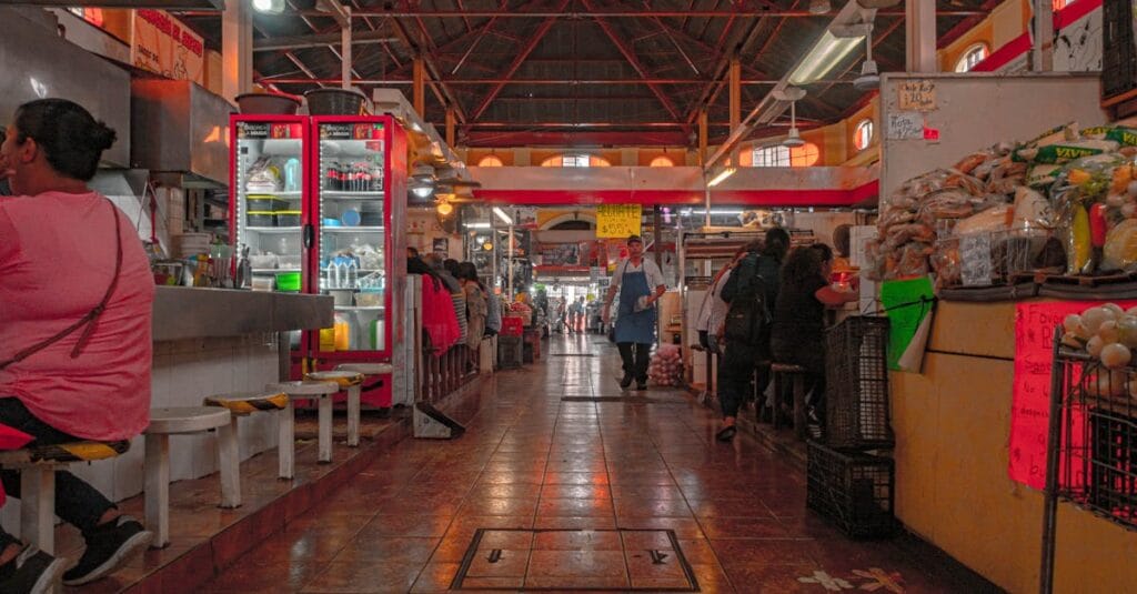 Indoor market scene bustling with food stalls and shoppers in a lively atmosphere.