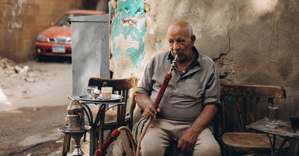 An elderly man sits outdoors enjoying shisha in Cairo, Egypt, reflecting local culture.