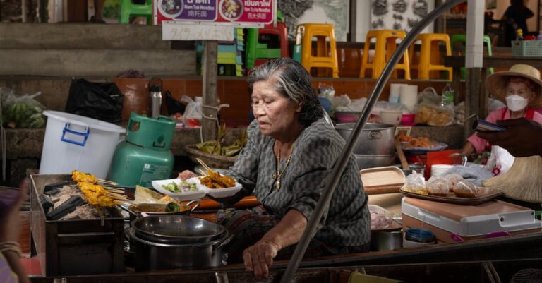Elderly woman cooking traditional Thai dishes at a bustling Bangkok street market.