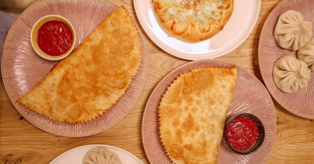 Flat lay featuring khinkali, fried pastry, and cheese bread with dips.