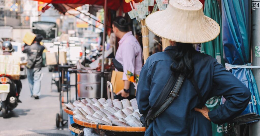 A busy Bangkok street market showing a vendor with fish under vibrant red umbrellas.