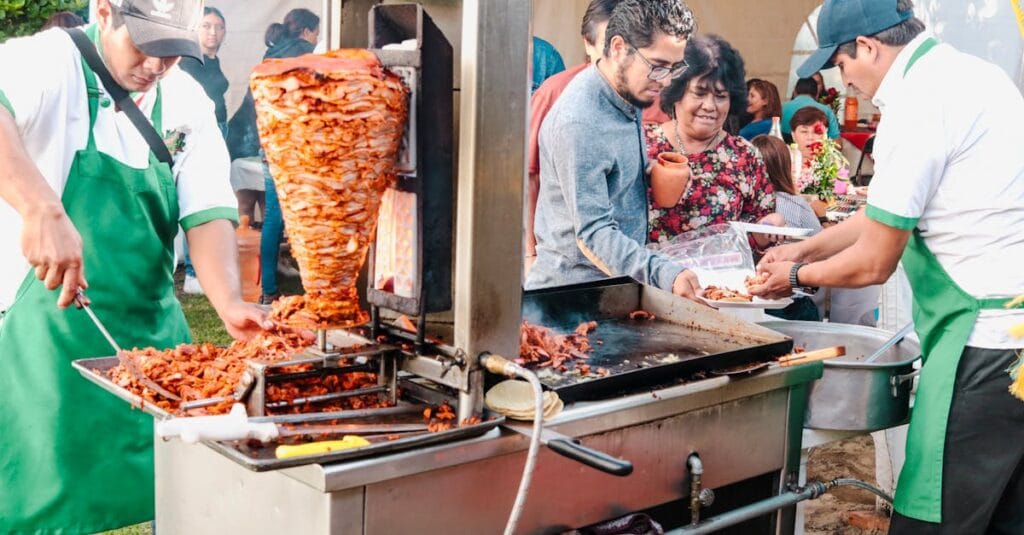 Vibrant scene at Mexican street food event featuring tacos al pastor preparation.