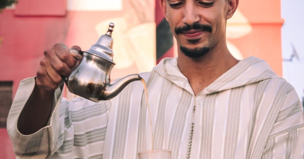 A man in Fez, Morocco, traditionally pouring tea outdoors, wearing a striped djellaba and a fez hat.