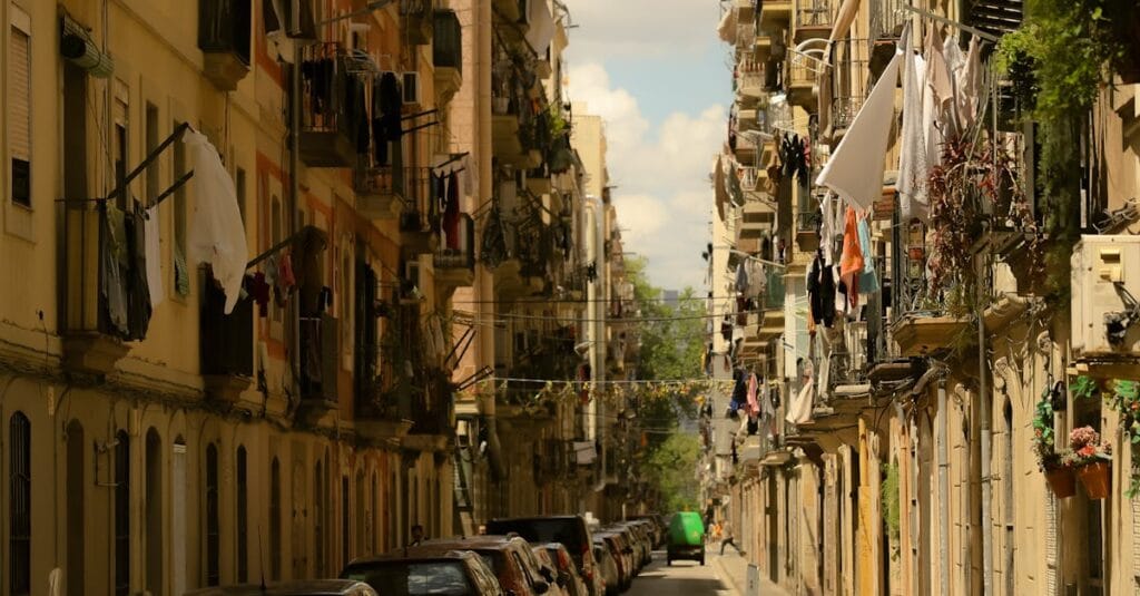 Charming narrow street in Barceloneta, Barcelona, with laundry hanging, cars parked, and classic architecture.