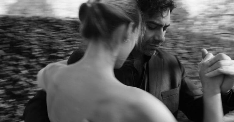 A couple gracefully dancing tango outdoors in a black and white photograph.