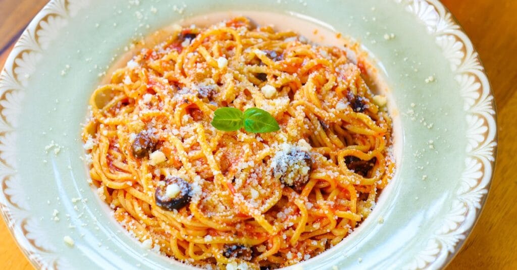 Close-up of a flavorful spaghetti dish topped with olives and parmesan cheese.
