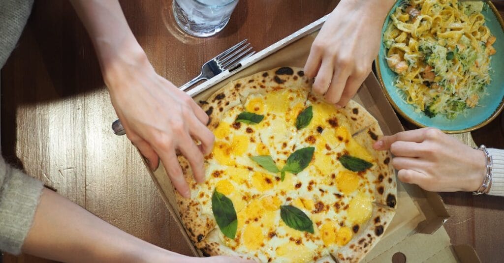 Top view of friends sharing a pizza and pasta meal at a cozy pizzeria.