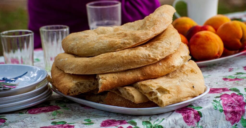 Platter of traditional Georgian bread with fresh peaches on a floral tablecloth, perfect for outdoor dining.