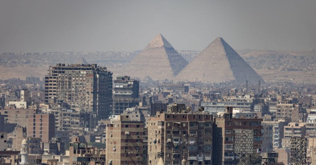 Aerial view of Cairo, Egypt, showcasing urban buildings with the iconic Pyramids of Giza in the background.