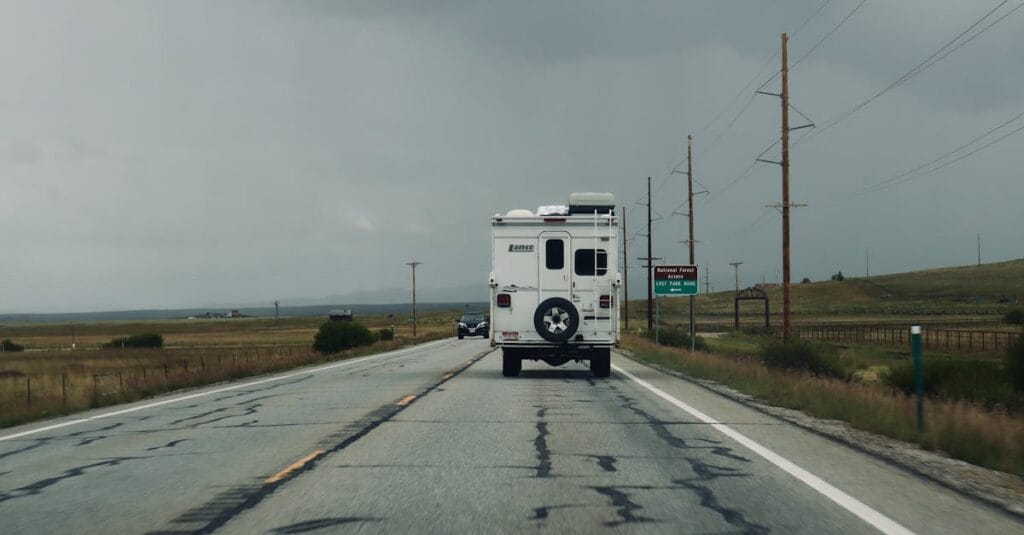A lone RV travels down a deserted road under a cloudy sky, evoking adventure.