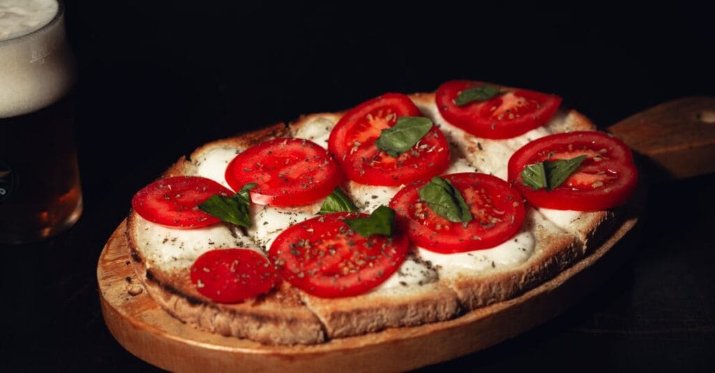 A delicious Caprese bruschetta with fresh tomatoes and basil served on a wooden board with a beer.