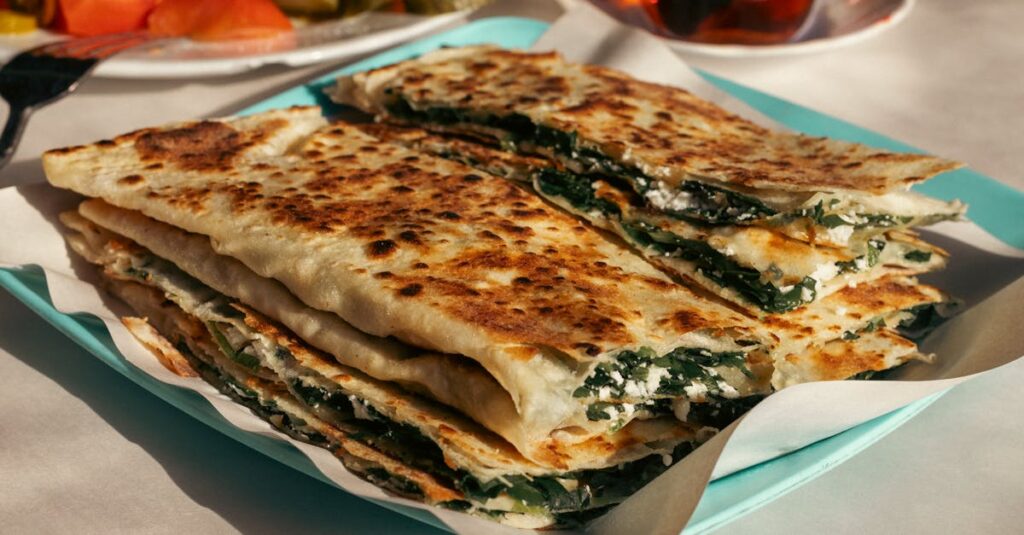 Close-up of freshly made Turkish Gözleme with spinach and cheese on a plate outdoors.