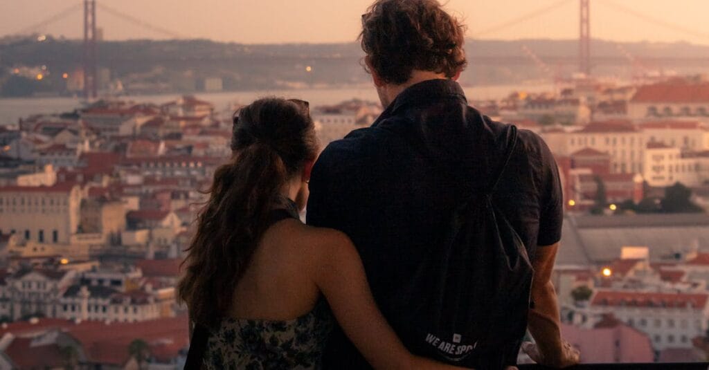 Couple enjoying a romantic sunset view overlooking Lisbon with the iconic 25 de Abril Bridge in the background.