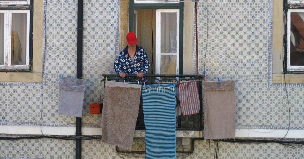 A woman stands on a Lisbon balcony with traditional Portuguese tiles, hanging laundry on a sunny day.