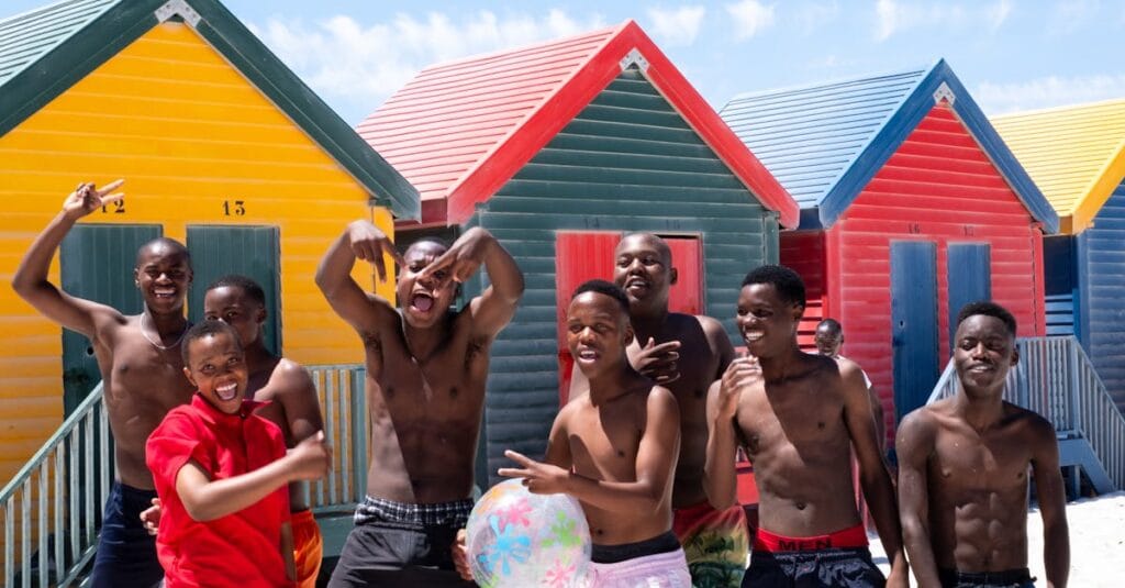 Lively group of friends having fun at colorful beach huts on a sunny day outdoors.