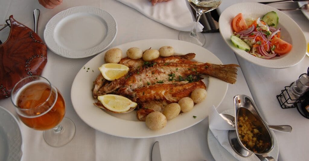 A tempting seafood platter with fish, potatoes, salad, and drinks on a dining table.