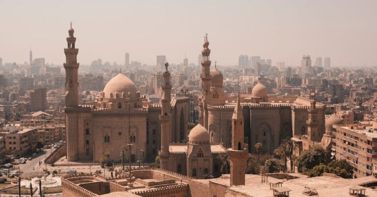 Aerial view of Cairo's historic mosques with a modern skyline backdrop under a clear sky.