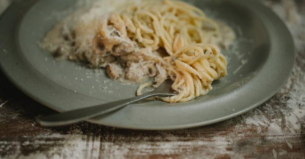Fork placed on plate with yummy fresh spaghetti pasta in cream mushroom sauce served on shabby table
