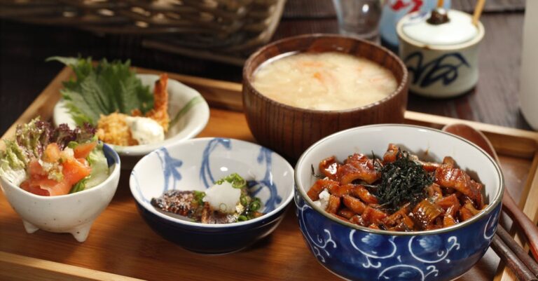 A beautifully arranged Japanese meal featuring rice bowl, miso soup, and side dishes on a wooden tray.