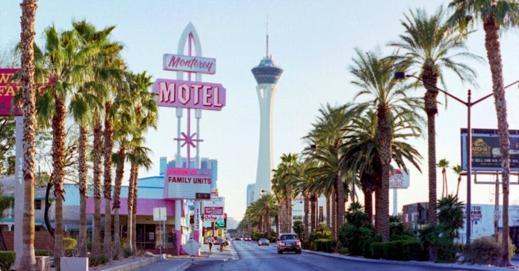 A street view of Las Vegas Boulevard showcasing the iconic Stratosphere Tower and a classic motel sign under clear skies.