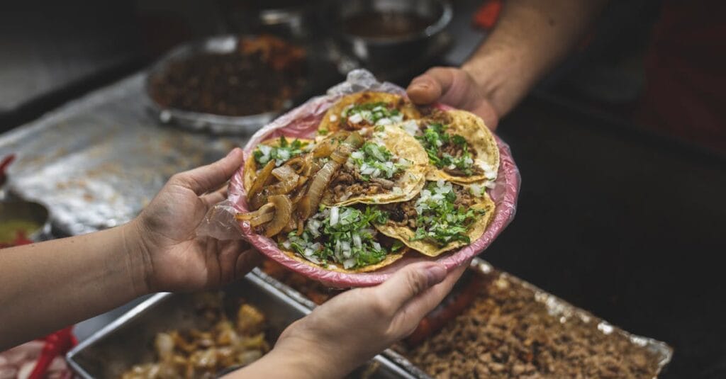 Freshly served authentic Mexican street tacos with onions and cilantro, handed over by vendor.